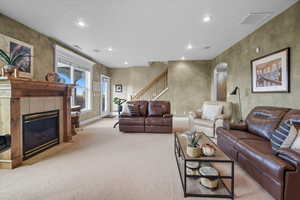 Living area with recessed lighting, a tiled fireplace, arched walkways, light colored carpet, and stairway