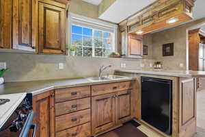 Kitchen with electric stove, black dishwasher, brown cabinetry, light countertops, and a peninsula