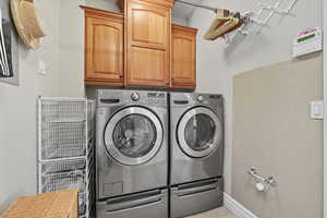 Washroom with cabinet space, washer and clothes dryer, and light tile patterned floors