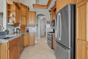 Kitchen with open shelves, appliances with stainless steel finishes, light countertops, arched walkways, and light tile patterned flooring