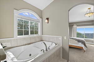 Ensuite bathroom featuring a whirlpool tub, vaulted ceiling, and carpet flooring
