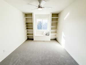 Empty room with light carpet, built in features, and ceiling fan