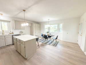 Kitchen with a center island, a breakfast bar, light countertops, pendant lighting, and light wood-style flooring