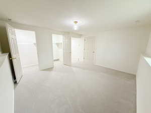 Unfurnished bedroom featuring a spacious closet, light colored carpet, and a textured ceiling