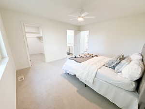 Bedroom with carpet, a walk in closet, a ceiling fan, and ensuite bathroom