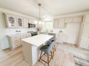 Kitchen with a breakfast bar area, a kitchen island, pendant lighting, light wood-style flooring, and appliances with stainless steel finishes