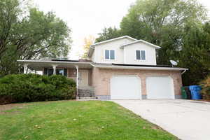 View of front of property with covered porch, a front yard, driveway, and brick siding