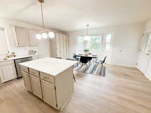 Kitchen with a kitchen island, stainless steel dishwasher, light countertops, light wood-style floors, and hanging light fixtures