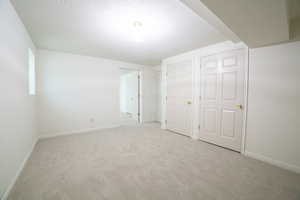 Unfurnished bedroom featuring light colored carpet, a textured ceiling, and two closets