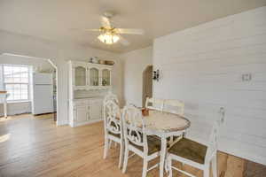 Dining room with arched walkways, light wood-type flooring, a ceiling fan, and wooden walls