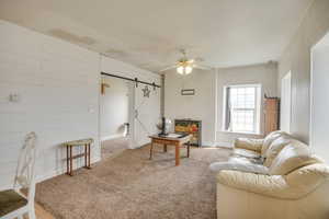 Living room with a barn door, a ceiling fan, carpet, and wood walls