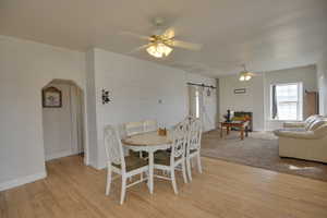 Dining area with a barn door, ceiling fan, light wood-style floors, and arched walkways
