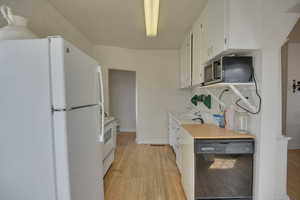 Kitchen featuring white appliances, white cabinets, light wood-style flooring, and light countertops