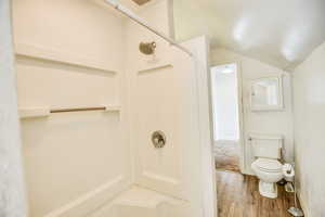 Full bath with wood finished floors, vaulted ceiling, and a shower