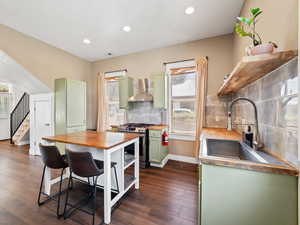 Kitchen featuring green cabinets, butcher block countertops, stainless steel gas stove, dark wood-style flooring, and decorative backsplash