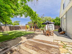 Fenced backyard featuring a storage unit, a patio area, outdoor dining space, and a pergola
