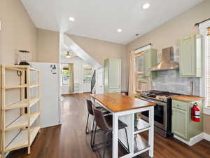 Kitchen with green cabinetry, wooden counters, gas stove, freestanding refrigerator, and dark wood-style floors