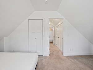 Bedroom with vaulted ceiling, light carpet, and a closet