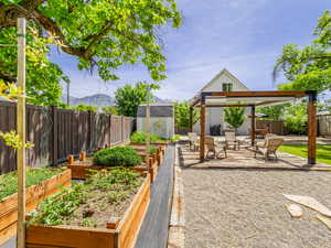 Fenced backyard featuring a vegetable garden, a storage unit, a deck with mountain view, a patio, and a pergola