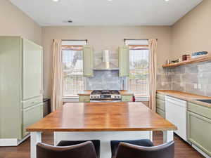 Kitchen featuring green cabinets, tasteful backsplash, wall chimney range hood, stainless steel range with gas cooktop, and recessed lighting