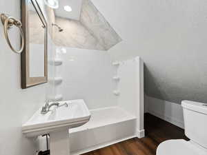 Full bath with dark wood finished floors, bathtub / shower combination, a textured ceiling, and vaulted ceiling