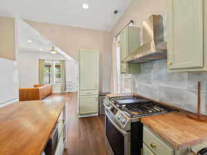 Kitchen with green cabinetry, stainless steel range with gas stovetop, wall chimney range hood, dark wood finished floors, and backsplash