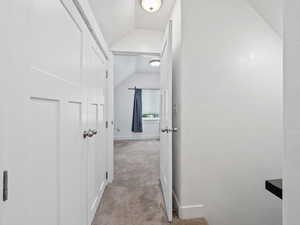 Hallway featuring vaulted ceiling and light colored carpet