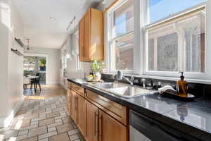 Kitchen with dark countertops, hanging light fixtures, stainless steel dishwasher, and brown cabinets