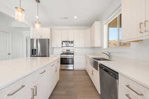Kitchen featuring stainless steel appliances, decorative light fixtures, dark wood finished floors, light stone counters, and recessed lighting