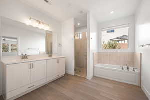 Bathroom featuring plenty of natural light, a bath, double vanity, light wood-style flooring, and recessed lighting