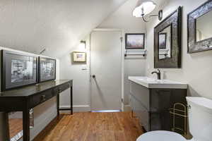 Half bath featuring a textured ceiling, light wood-style flooring, vaulted ceiling, and vanity