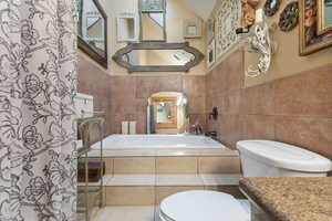 Bathroom with a bath, tile walls, a shower with shower curtain, and vanity