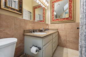 Full bath with tile walls, double vanity, and light tile patterned floors