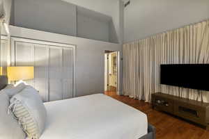 Bedroom featuring dark wood-style flooring, a high ceiling, and a closet