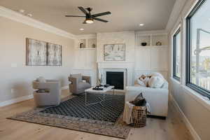 Living room featuring a large fireplace, crown molding, light wood-style floors, ceiling fan, and built in features