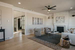 Living area with a barn door, light wood-type flooring, a fireplace, a ceiling fan, and built in features