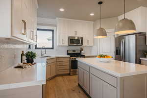 Kitchen featuring appliances with stainless steel finishes, a kitchen island, tasteful backsplash, light wood-style flooring, quartz countertops and recessed lighting