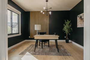 Office featuring light wood-type flooring, custom woodwork on wall and a contemporary chandelier