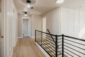 Corridor with access to 2 more bedrooms, an upstairs landing and light wood-type flooring, custom rod iron railing, and custom lighting