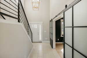 Foyer featuring custom rod iron railing, custom lighting, contemporary sliding doors into office, a chandelier, stairway, and a high ceiling
