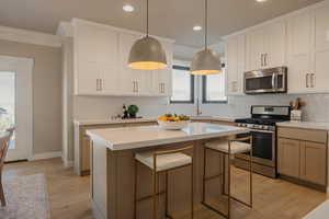 Kitchen featuring backsplash, stainless steel appliances, light wood-style flooring, pendant lighting, quartz countertops and crown molding