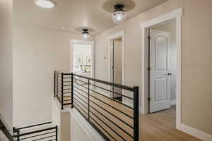 Corridor leading to 1 bedroom, full bath & Primary suite with an upstairs landing, light wood-style flooring, custom rod iron railing, and custom lighting