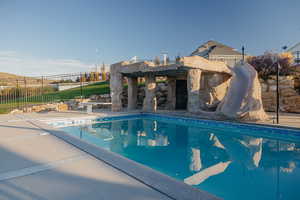 View of swimming pool featuring a massive Grotto with Slide & Waterfall.  Pool features a diving board & built-in basketball hoop!