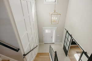 Foyer with custom woodwork on wall,  contemporary sliding doors, a high ceiling, light wood-style flooring, a chandelier, and stairs
