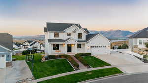 Modern inspired farmhouse featuring board and batten siding, concrete driveway, a mountain view, a front lawn, and a shingled roof