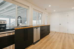 Kitchen featuring appliances with stainless steel finishes, dark cabinets, recessed lighting, light wood finished floors, and modern cabinets
