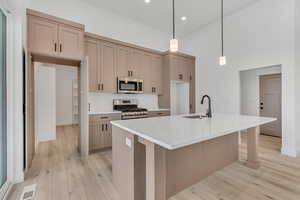 Kitchen featuring appliances with stainless steel finishes, light stone counters, pendant lighting, a kitchen island with sink, and light wood-type flooring