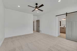 Unfurnished bedroom featuring a barn door, light carpet, a ceiling fan, recessed lighting, and ensuite bathroom