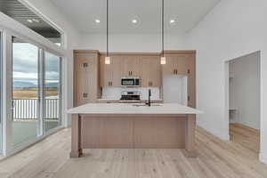 Kitchen with stainless steel appliances, hanging light fixtures, light stone counters, a center island with sink, and recessed lighting