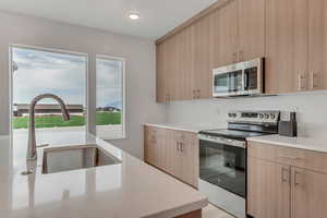 Kitchen with appliances with stainless steel finishes, modern cabinets, light stone counters, light brown cabinetry, and recessed lighting